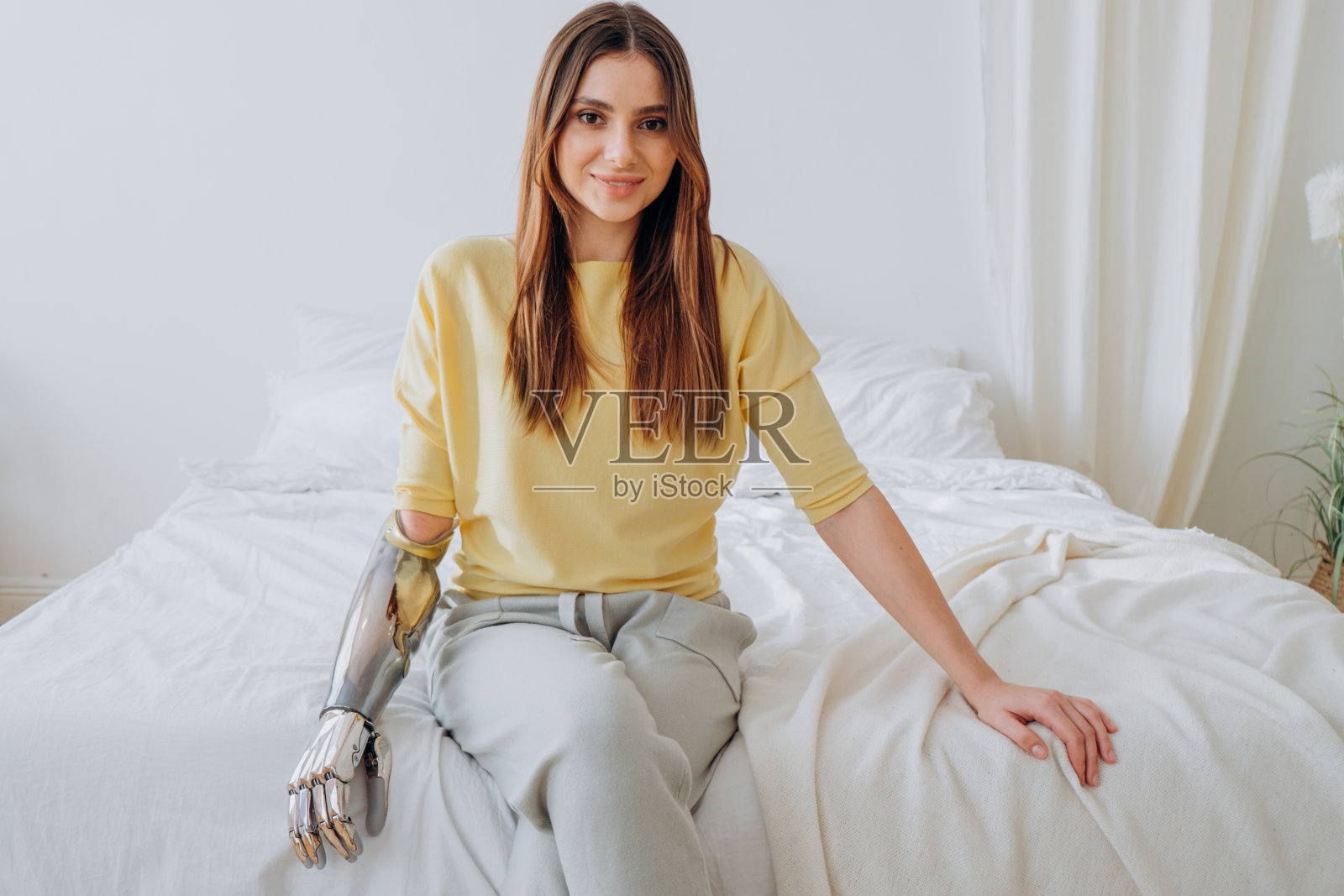 一个快乐的女人戴着仿生假肢坐在柔软的大床上照片摄影图片