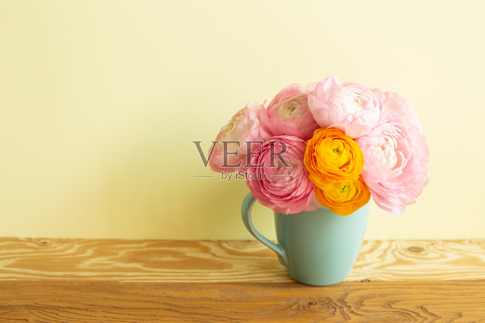 木桌上放着一瓶毛茛花。黄色背景照片摄影图片