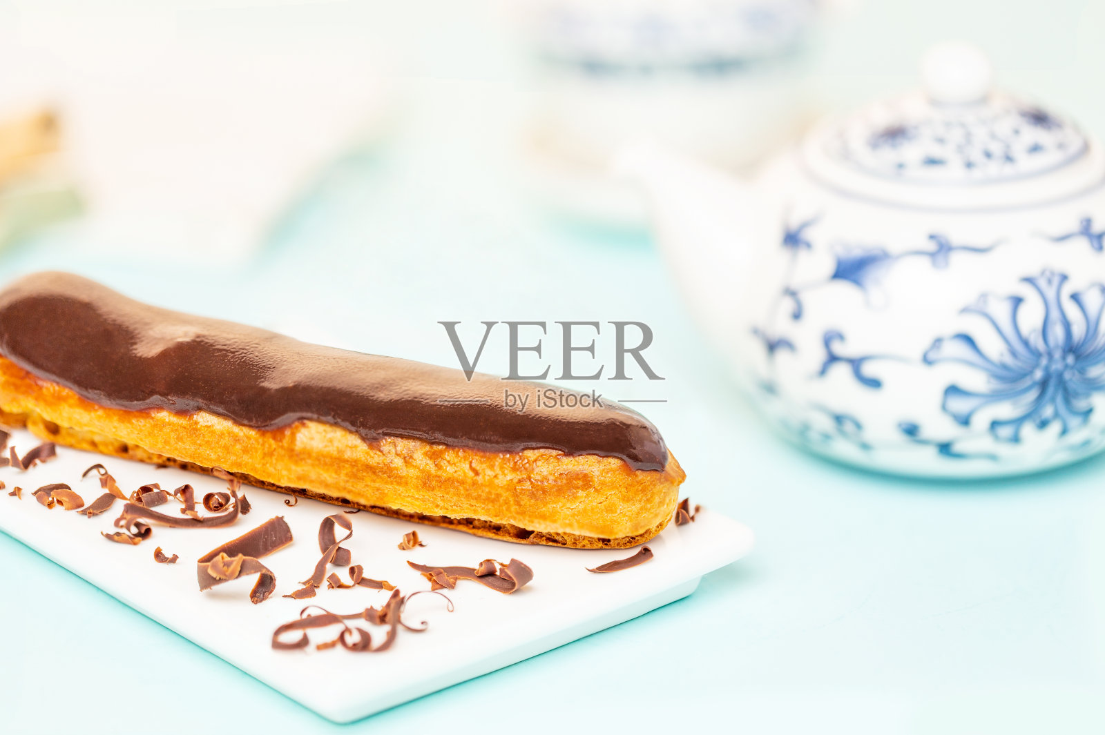 白色盘子上涂有巧克力屑的法式巧克力泡芙，旁边放着中国茶壶，以浅蓝色为背景。照片摄影图片