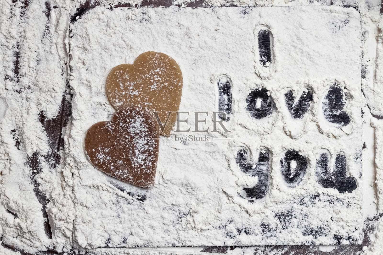 两颗不同的心，亮的和暗的，用生的曲奇面团做成的，还有在白色面粉覆盖的黑色桌子上手绘的“我爱你”照片摄影图片