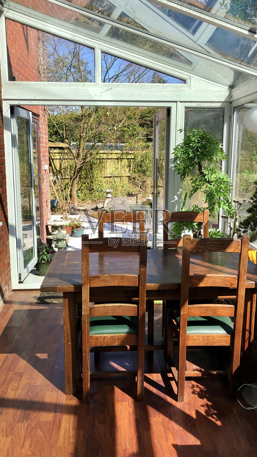 室内的玻璃温室，用餐区，深色木质餐桌和椅子，敞开的门可以看到家庭花园照片摄影图片