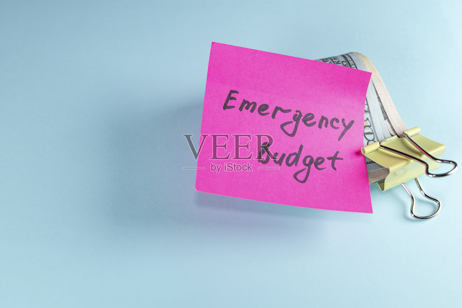 用纸夹夹在淡蓝色背景上的美元，上面写着紧急基金:设定储蓄目标的概念照片摄影图片