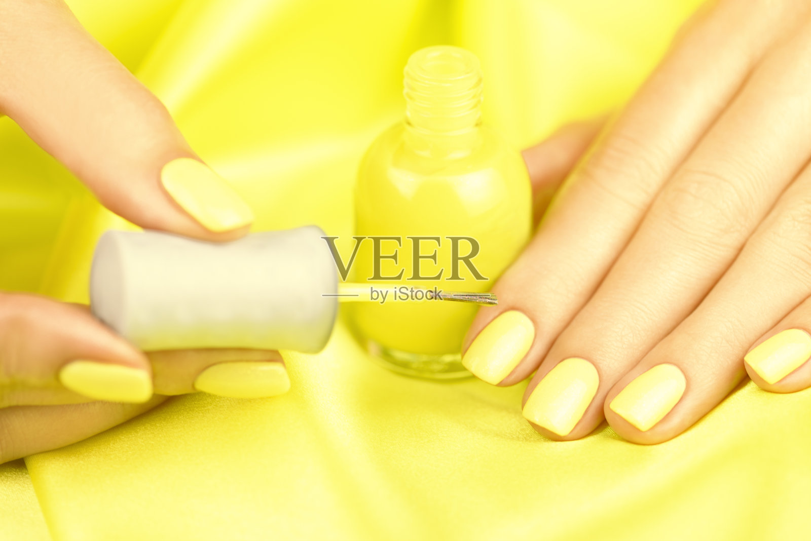 女性的手与黄色的美甲在黄色的丝绸背景。一个女人用黄色指甲油涂指甲。照片摄影图片