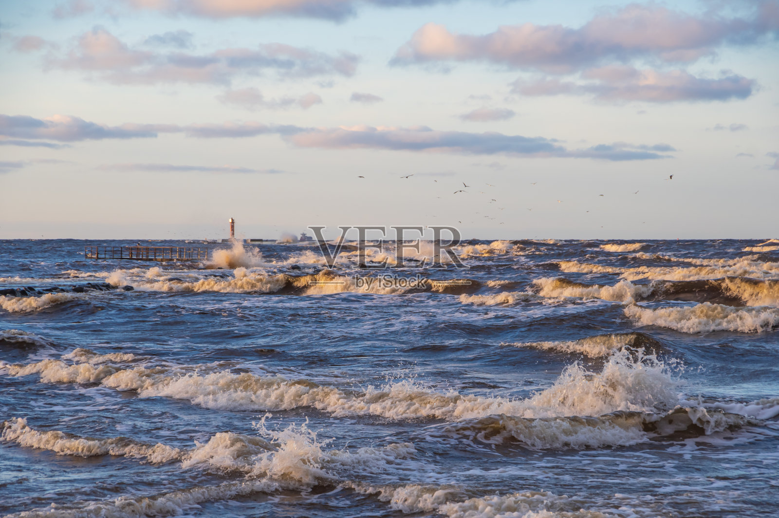 傍晚波罗的海波浪起伏，天空多云。地平线上的橙色曼加拉灯塔。照片摄影图片
