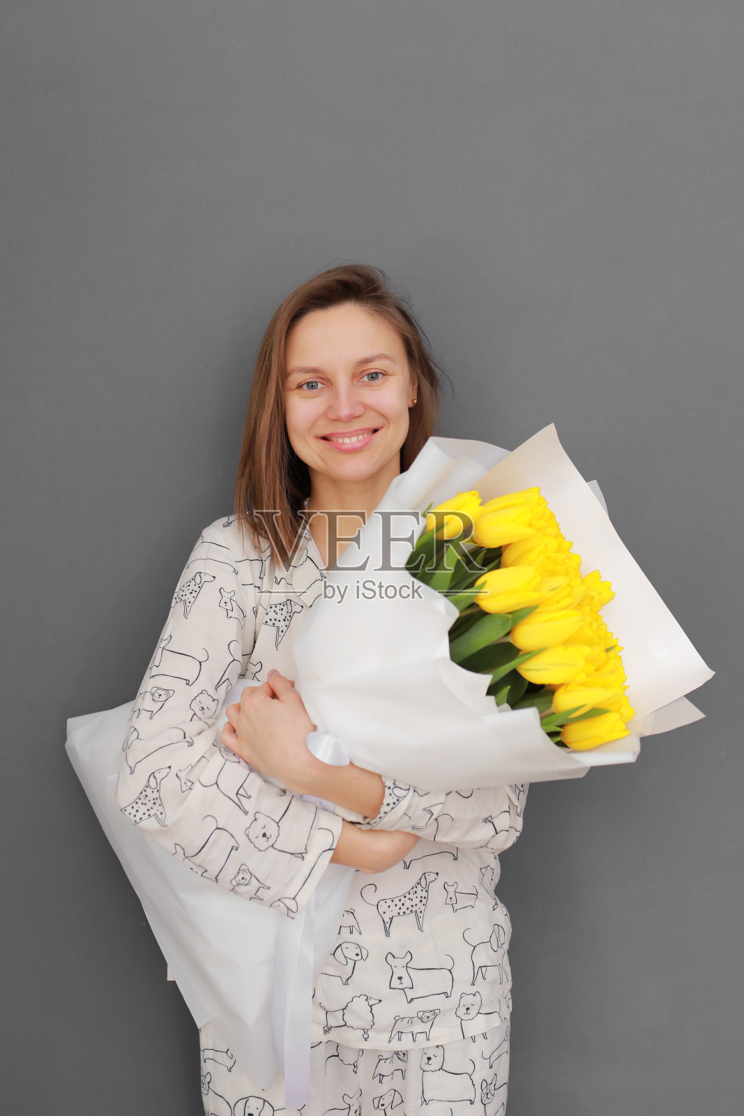 非常漂亮的年轻女子拿着一束又大又漂亮的新鲜的黄色郁金香花在灰色的墙壁背景上。国际妇女节照片摄影图片