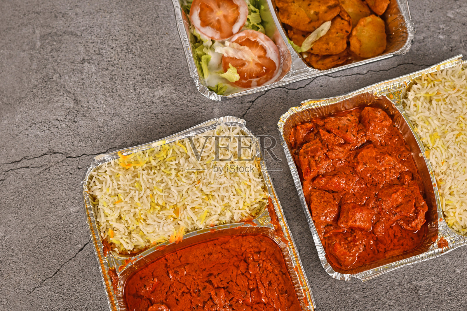 装有印度外卖食物的托盘，里面有红色的印度泥锅拌饭和米饭照片摄影图片