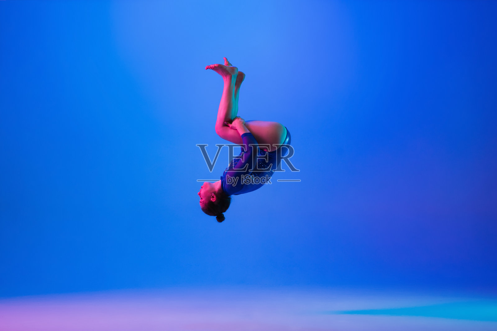 年轻柔顺的女孩孤立在蓝色的工作室背景。年轻的女模特在练习艺术体操。锻炼身体的灵活性和平衡性。照片摄影图片