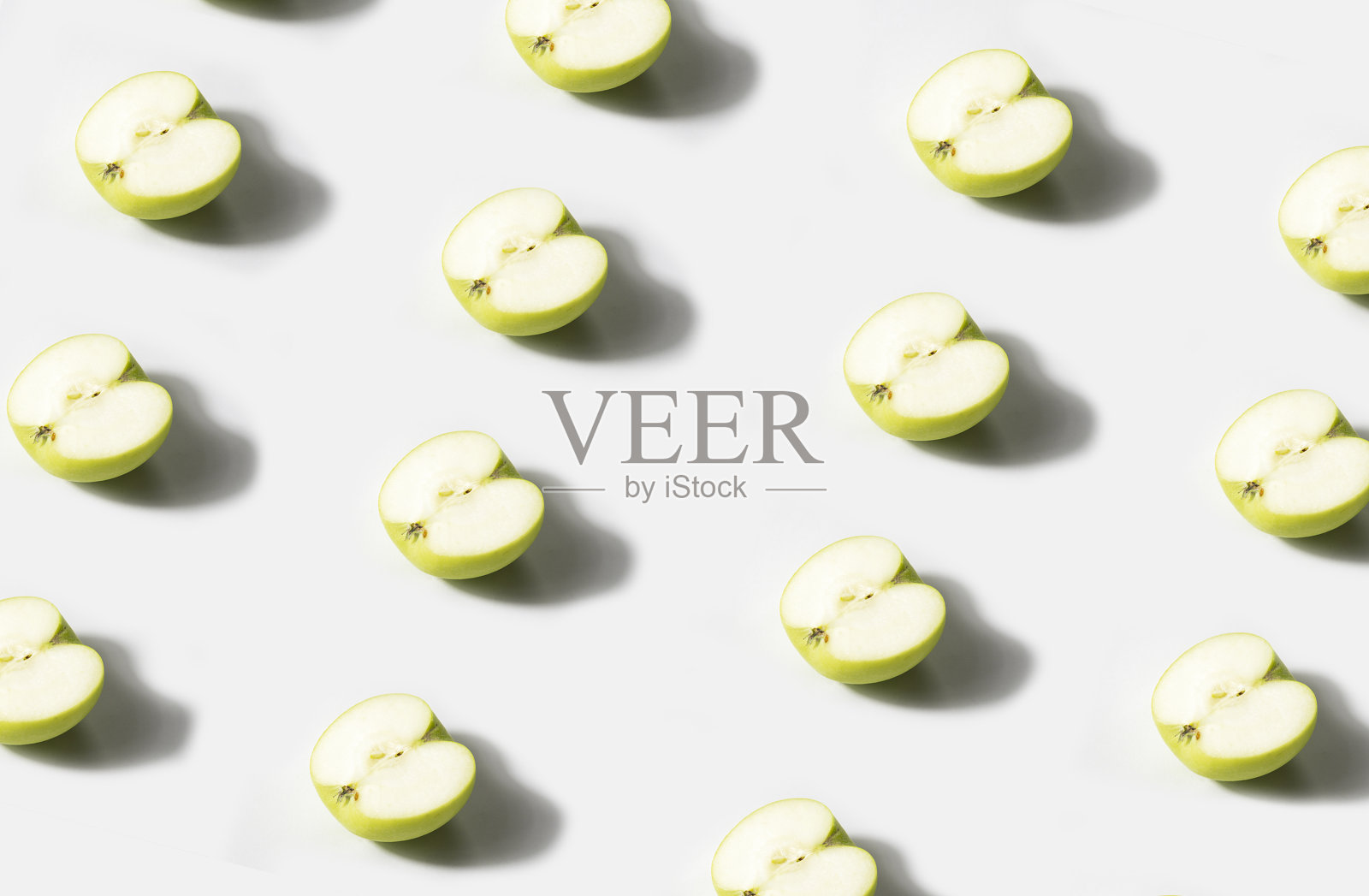 切了一半的青苹果在白色的背景上排成一排。苹果的影子形成一个心形照片摄影图片