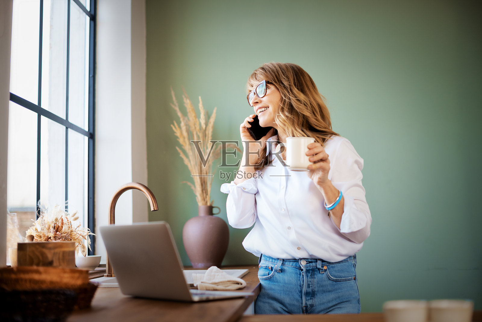 炙手可热的中年妇女在家工作时使用手机和笔记本电脑照片摄影图片