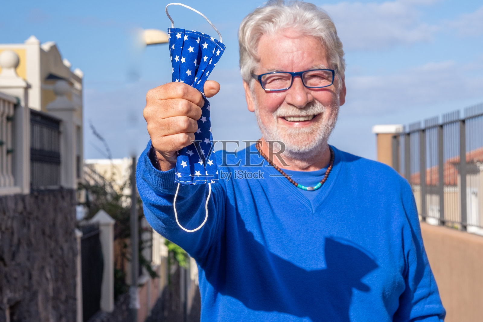 快乐的老人已经接种了抗冠状病毒感染，手拿防护口罩在户外微笑。散焦的人照片摄影图片