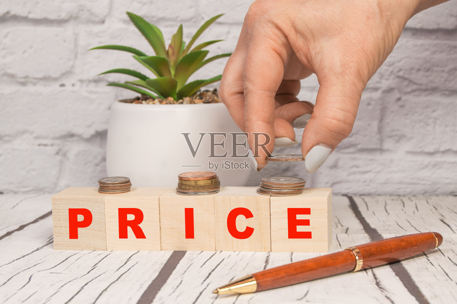 价格、金钱、金融或储蓄的概念通过使用一个带有字母的立方体木块，手将硬币折叠在一个轻木桌上照片摄影图片