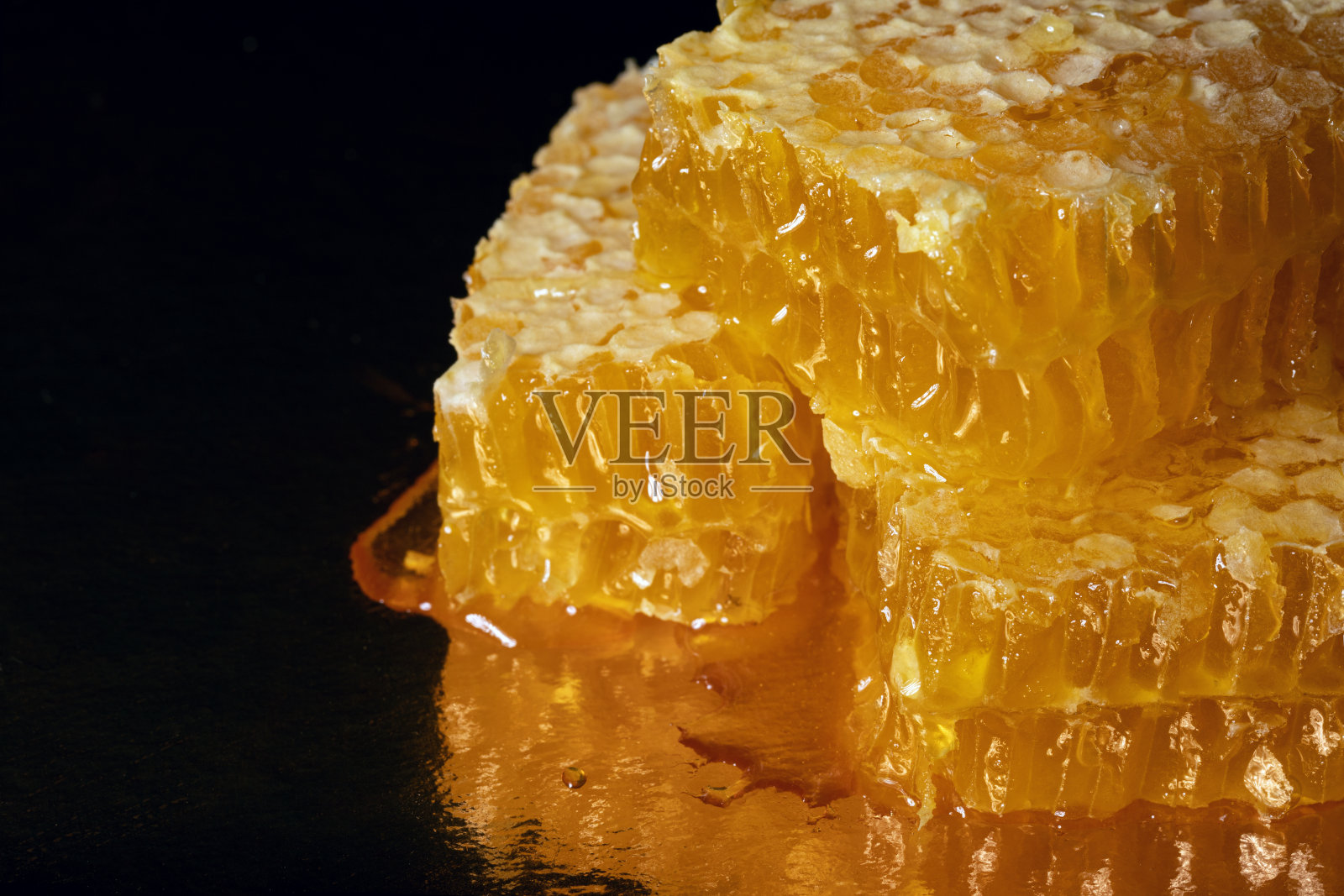 金色的新鲜蜂房与蜂蜜滴在黑暗的背景照片摄影图片