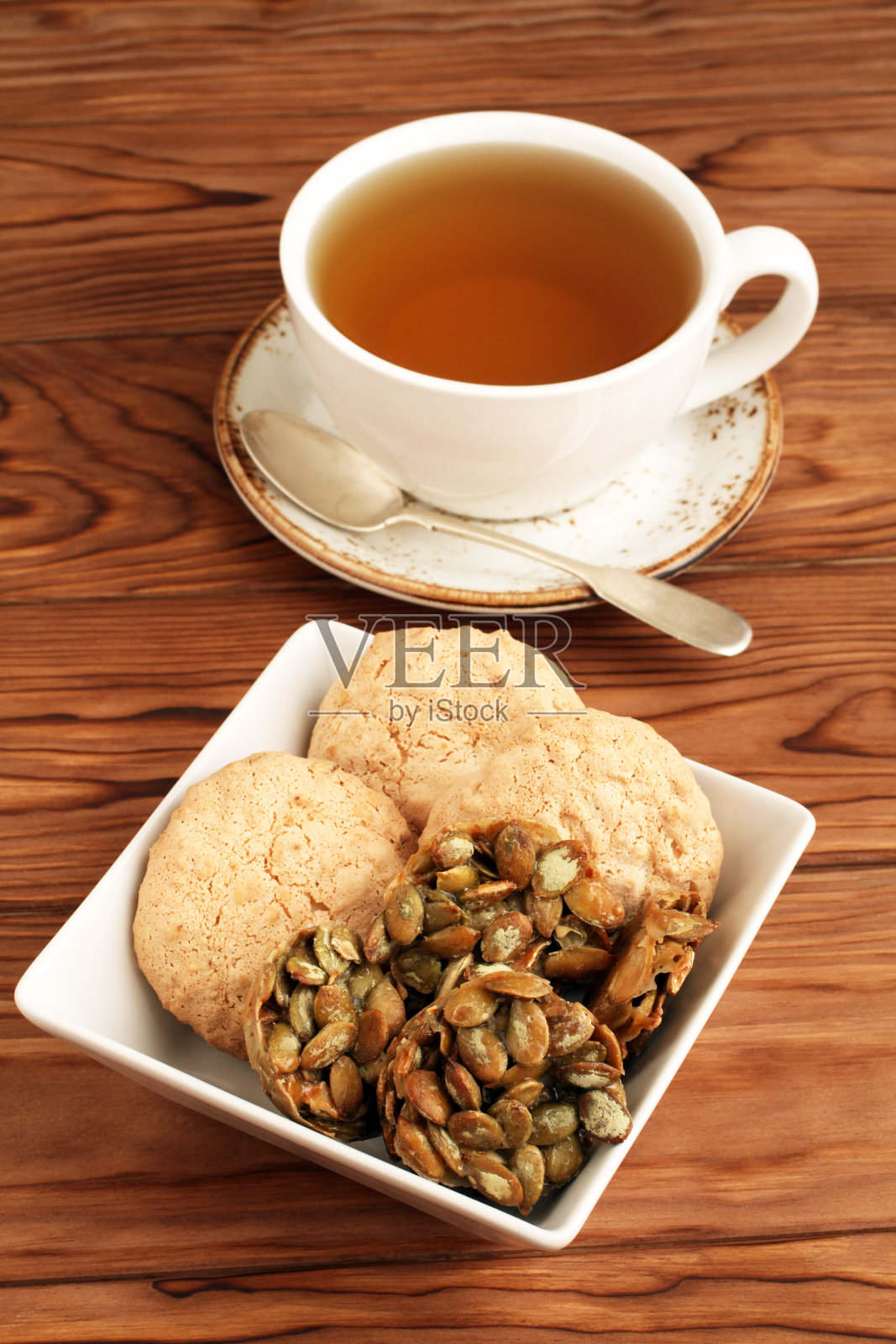 杏仁饼干和糖衣南瓜子饼干放在一个方碗里，一杯绿茶放在一张木桌上。特写镜头照片摄影图片