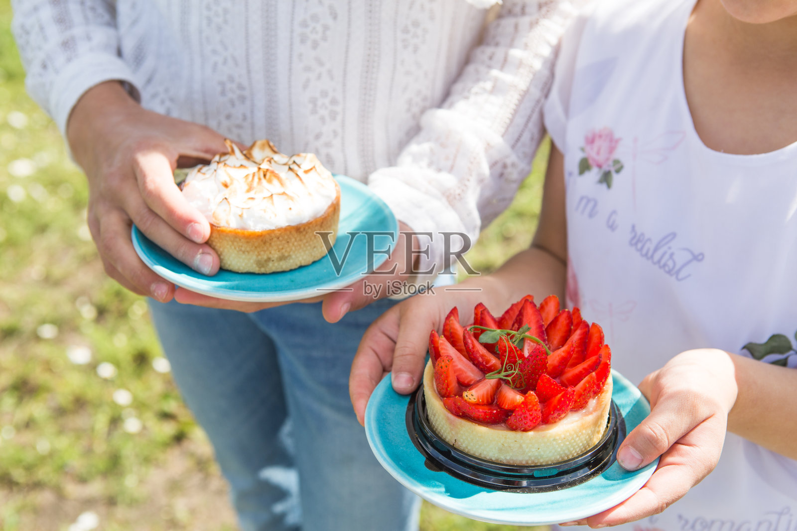 小女孩在外面吃草莓馅饼。自制素食挞与浆果，如蓝莓，树莓和草莓在春天与盛开的树枝在女人的手中。春季或夏季野餐概念照片摄影图片