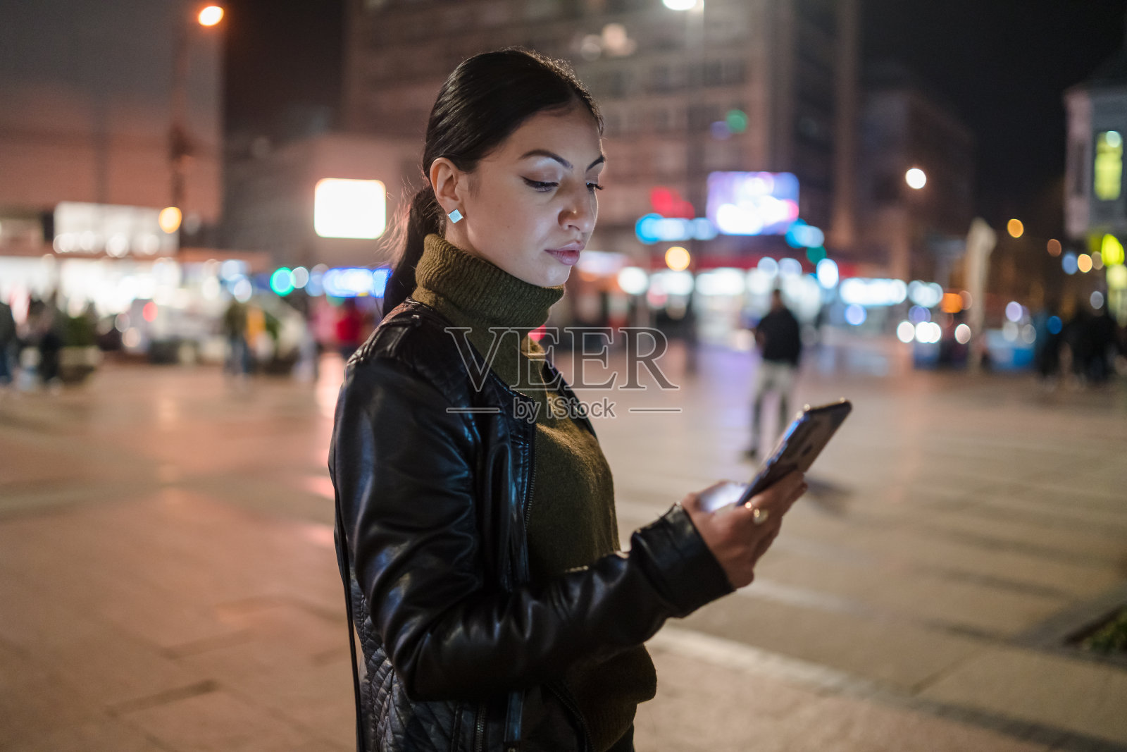 一名年轻女子在市中心晚上用智能手机拍照照片摄影图片