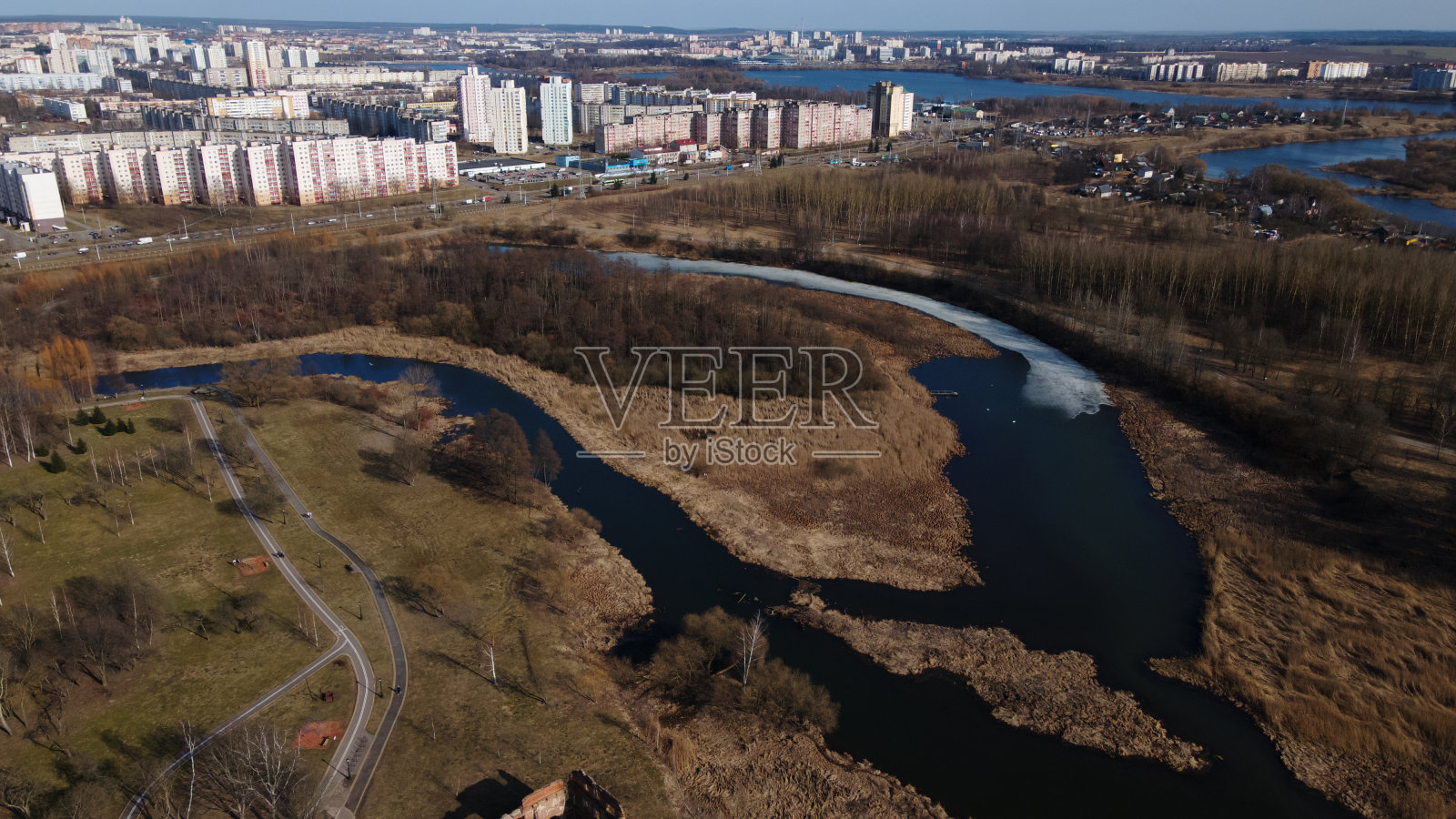 在春天飞过城市公园。有冰残的河流清晰可见。远处有多层的城市建筑。照片摄影图片