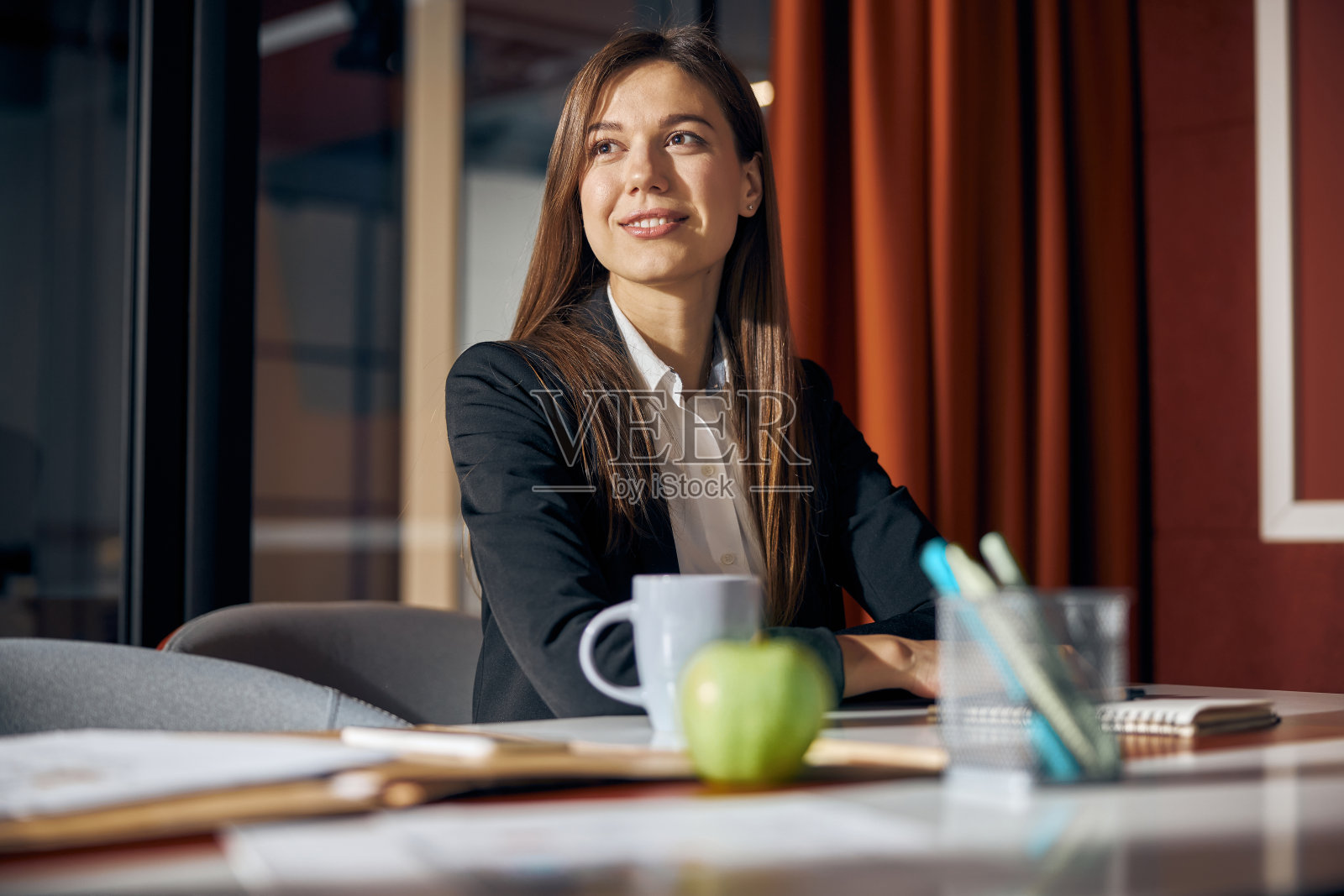 深思熟虑的女商人坐在桌旁，眼睛望向别处照片摄影图片