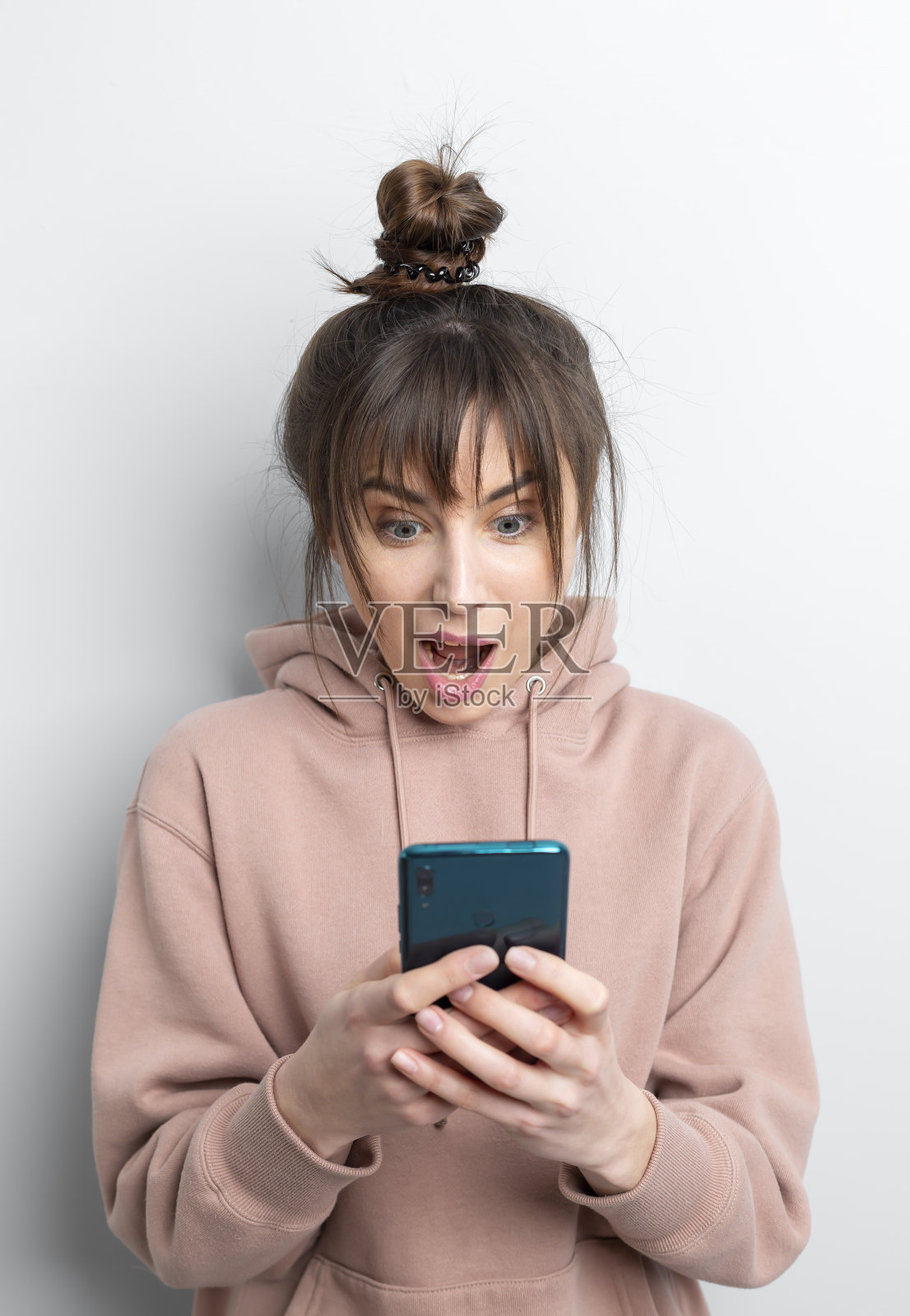 一个年轻女子高兴地被她在手机上看到的新闻震惊了。女孩欣喜地看着智能手机屏幕上的惊喜。照片摄影图片