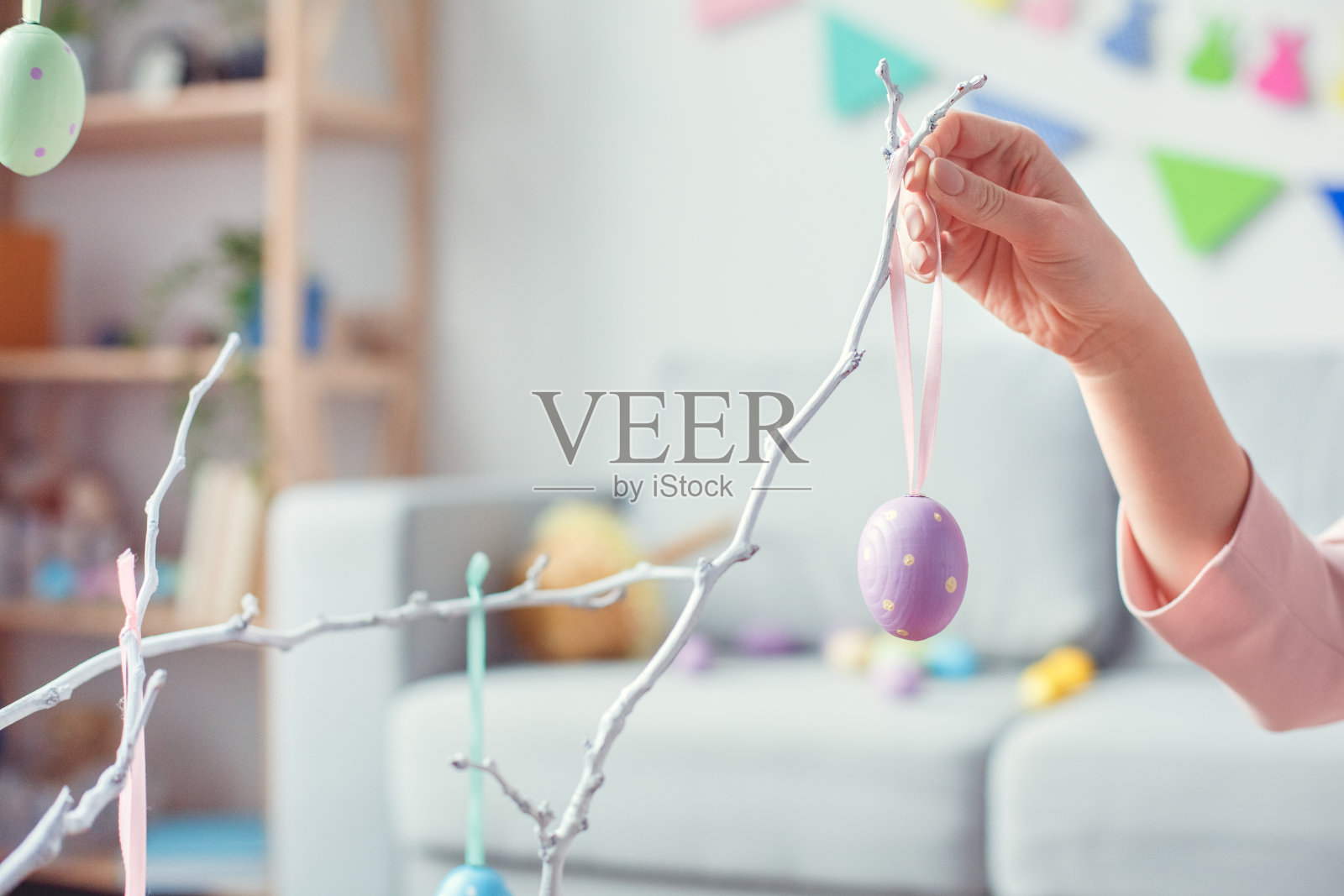 年轻妇女在家庆祝复活节的概念是把鸡蛋挂在树上照片摄影图片