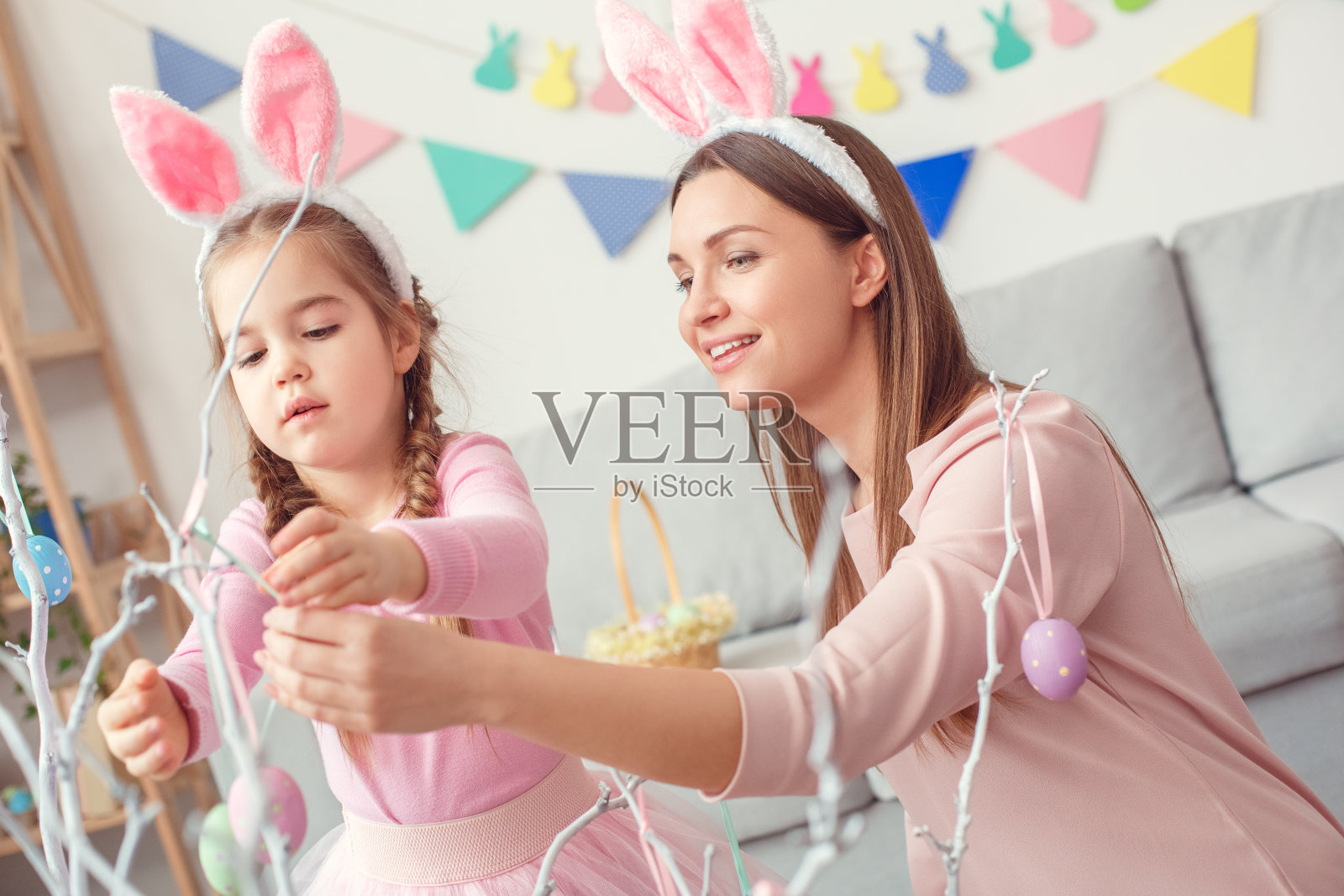 妈妈和女儿在兔子耳朵里一起在家构思复活节彩蛋挂在树上照片摄影图片