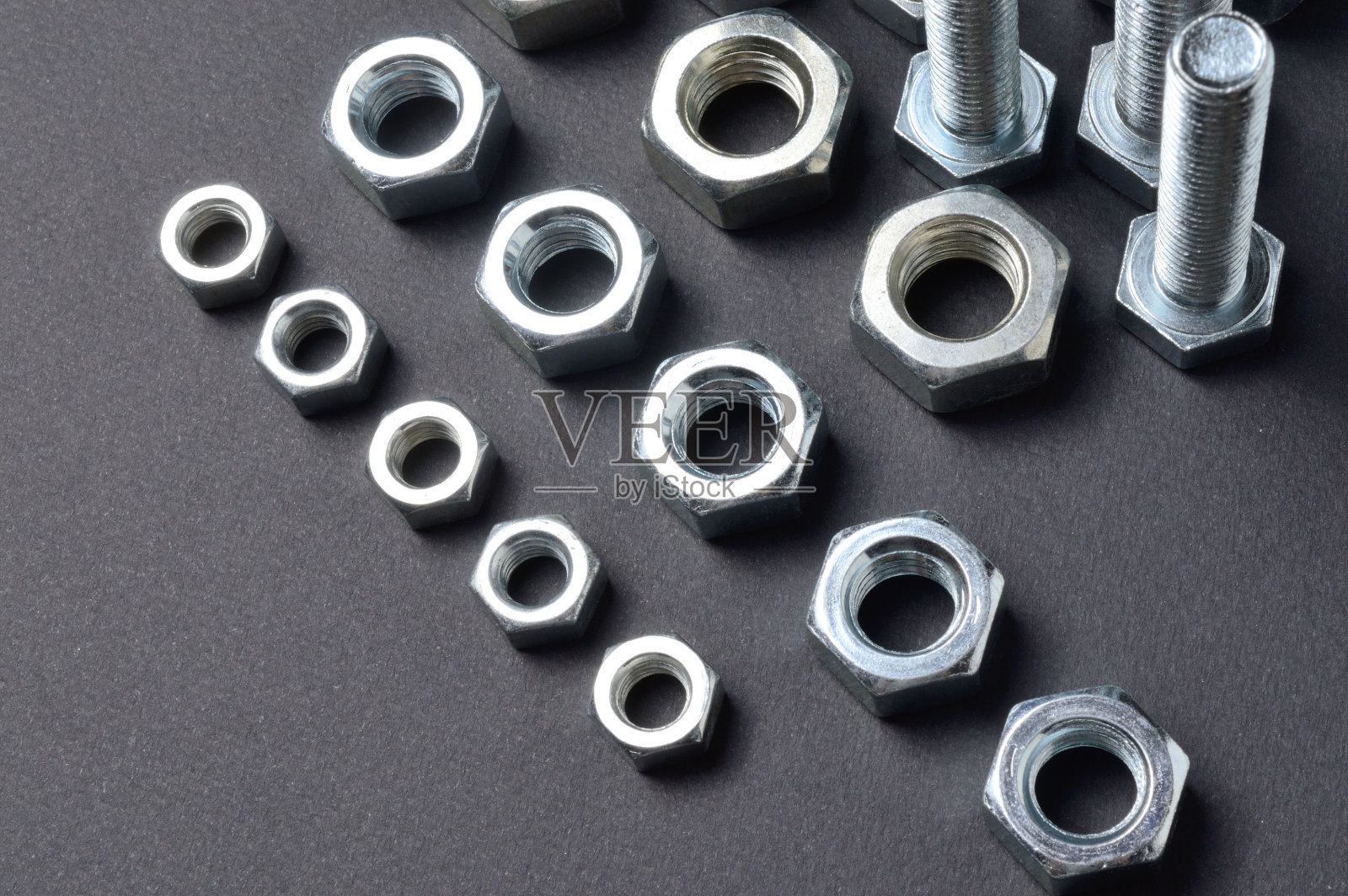 不同尺寸的新铬螺母和螺栓摆放在黑暗的背景下。特写镜头。照片摄影图片