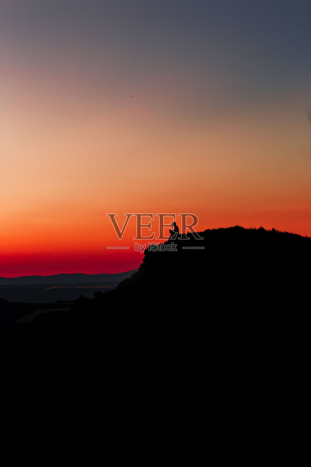 红色日落与山的剪影。日落时山上的一个人。旅行者在岩石上挥手。照片摄影图片