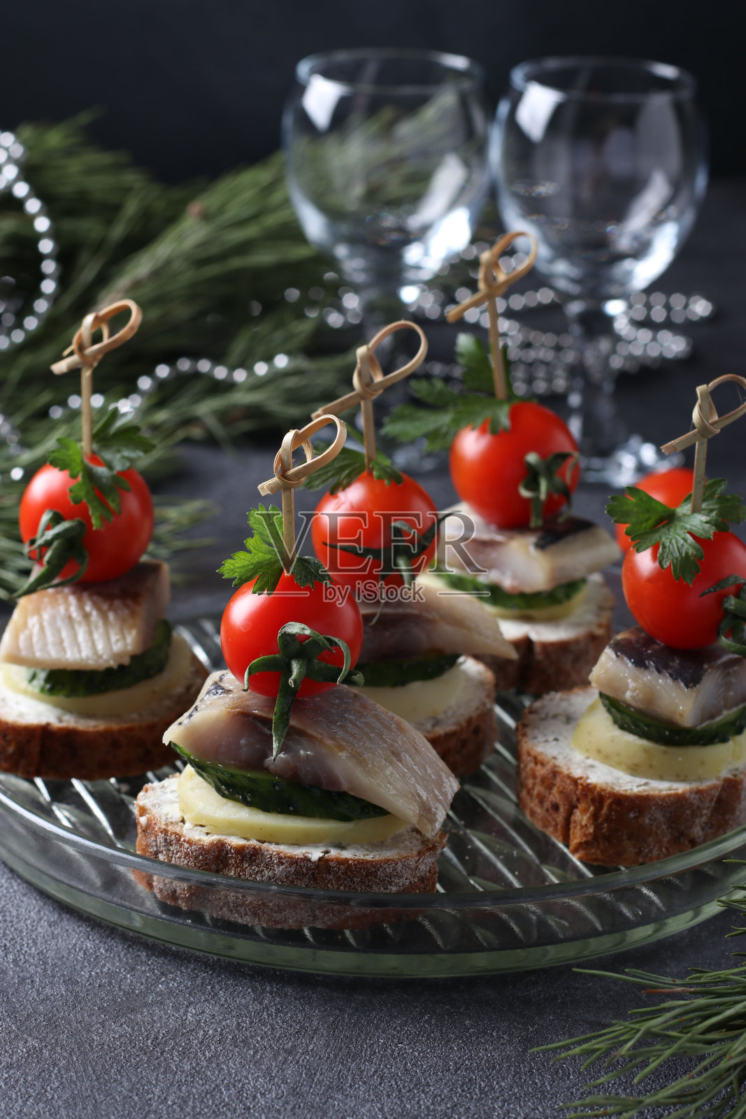 以咸鲱鱼，黄瓜，煮土豆，樱桃番茄和黑橄榄搭配黑麦面包丁，灰色背景。特写镜头照片摄影图片