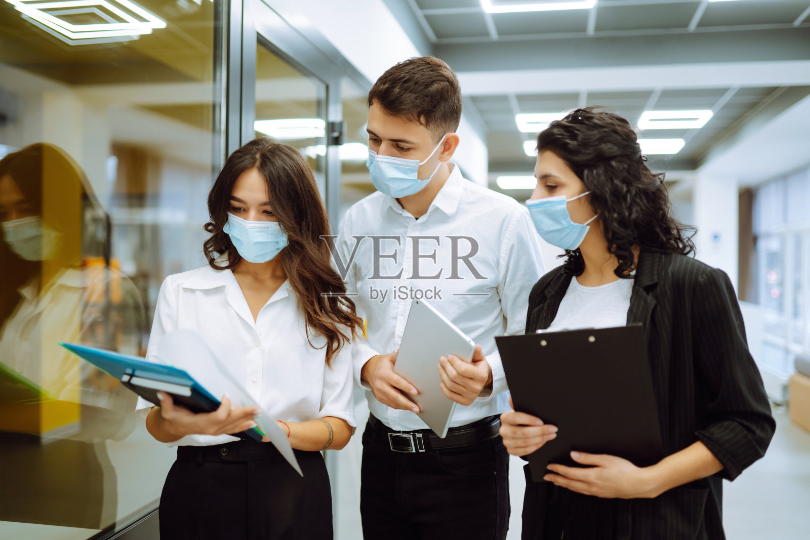 同事们戴着防护口罩一起讨论工作问题。照片摄影图片