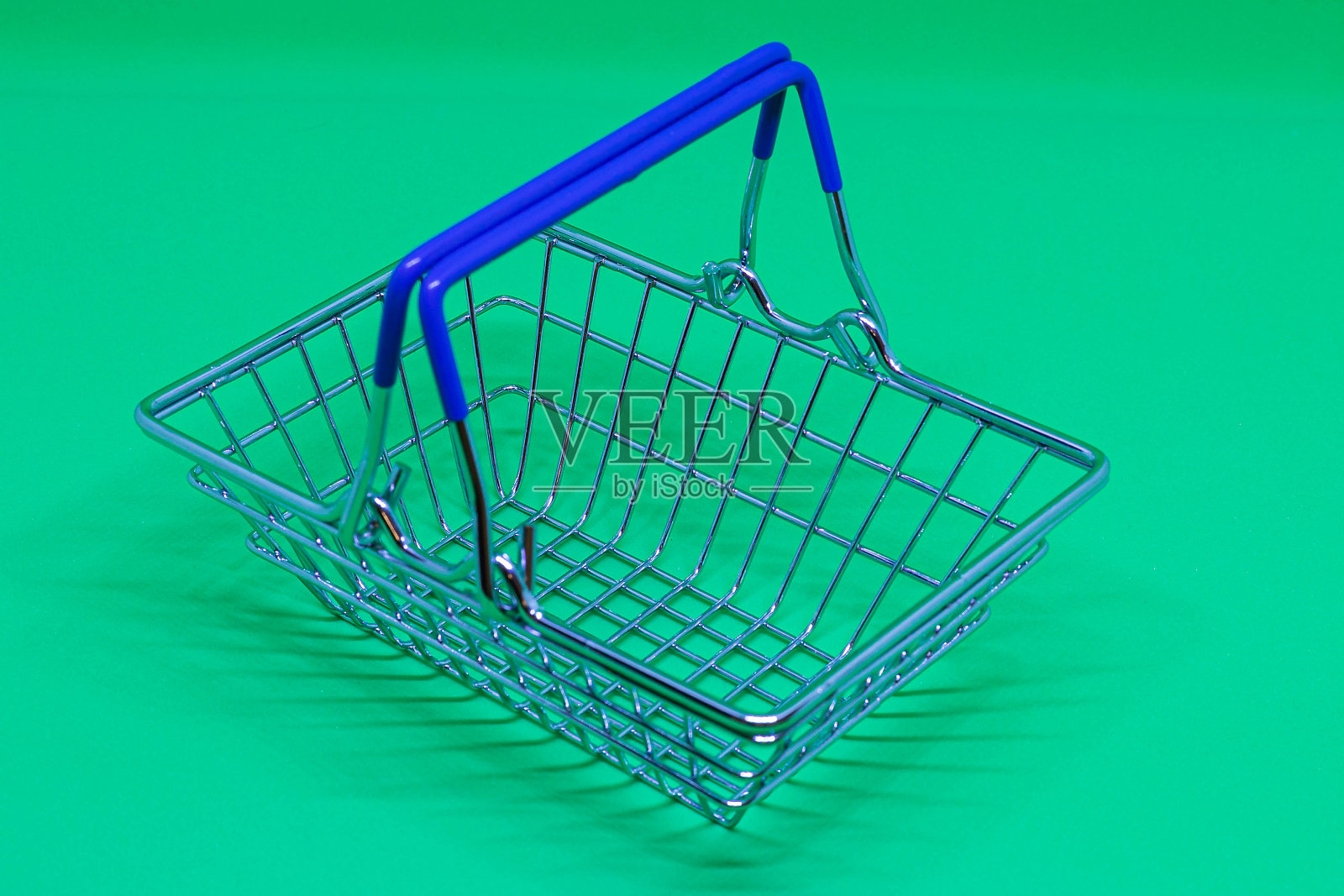 空迷你玩具自助购物篮与蓝色把手孤立在绿色背景。照片摄影图片