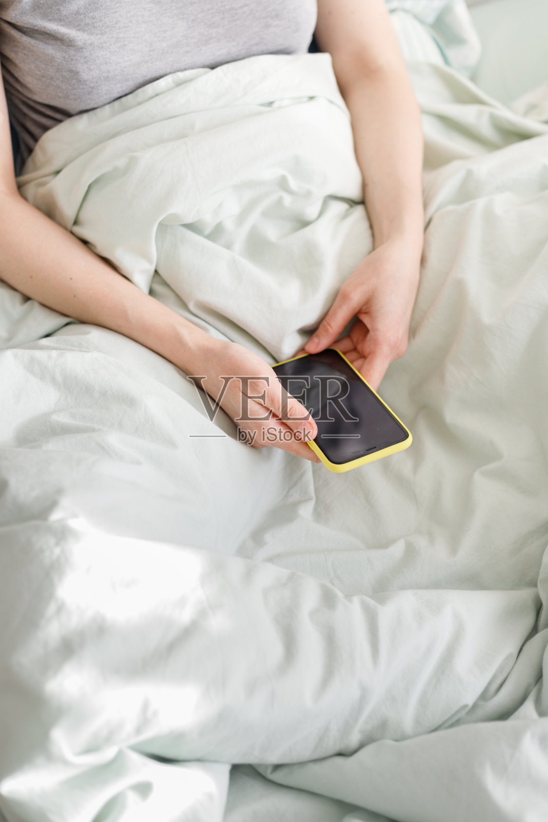 早上好，阳光明媚的一天，白种女人在看短信，手里拿着一个黄色的手机照片摄影图片