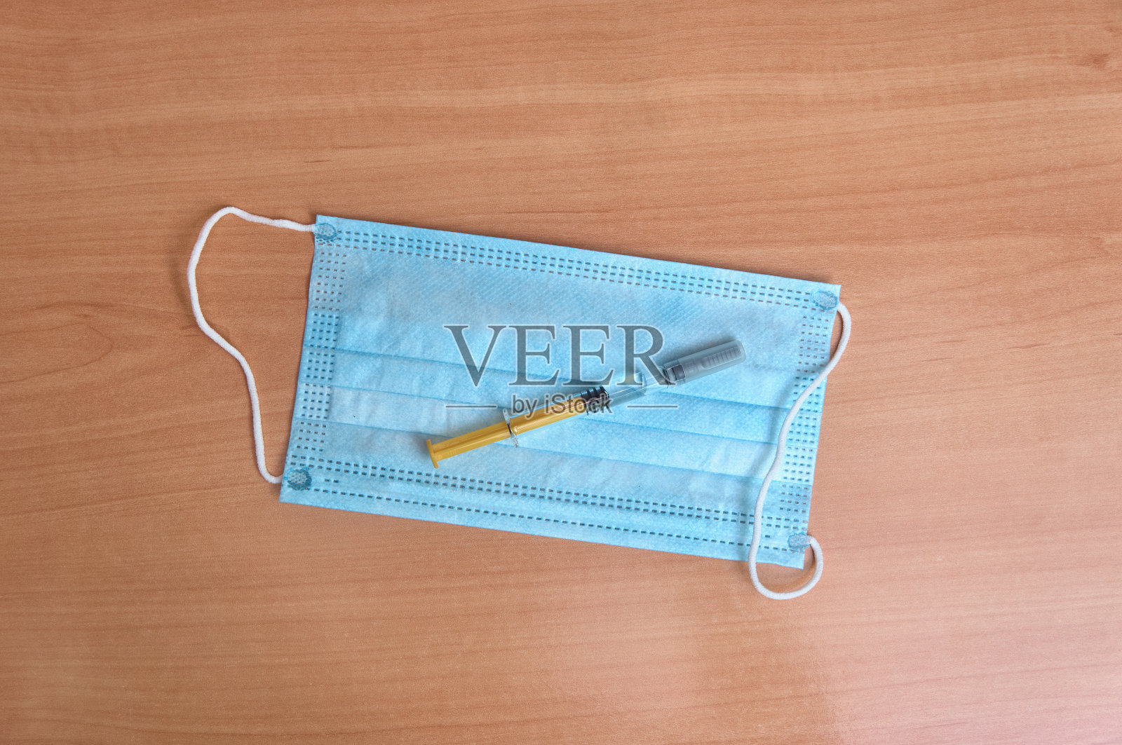 蓝色防护口罩和注射器放在木桌上。冠状病毒疫苗的概念。照片摄影图片