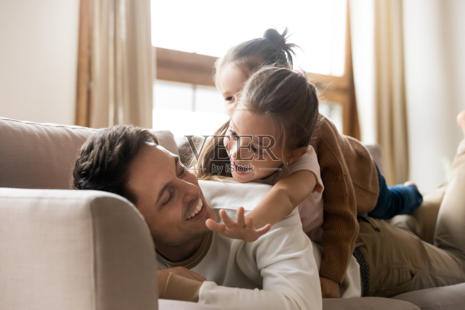 快乐的父亲和两个小女儿躺在沙发上照片摄影图片