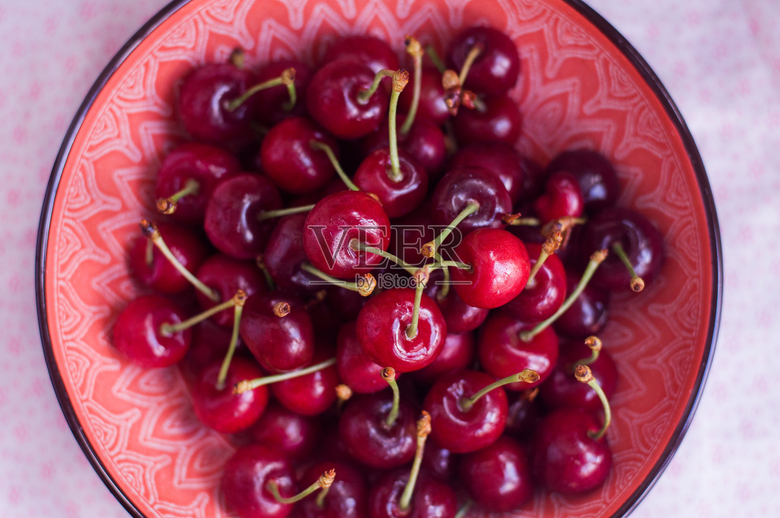 女人的手握着一根小枝，上面有一颗年轻甜美的樱桃。红粉色盘子里的樱桃照片摄影图片