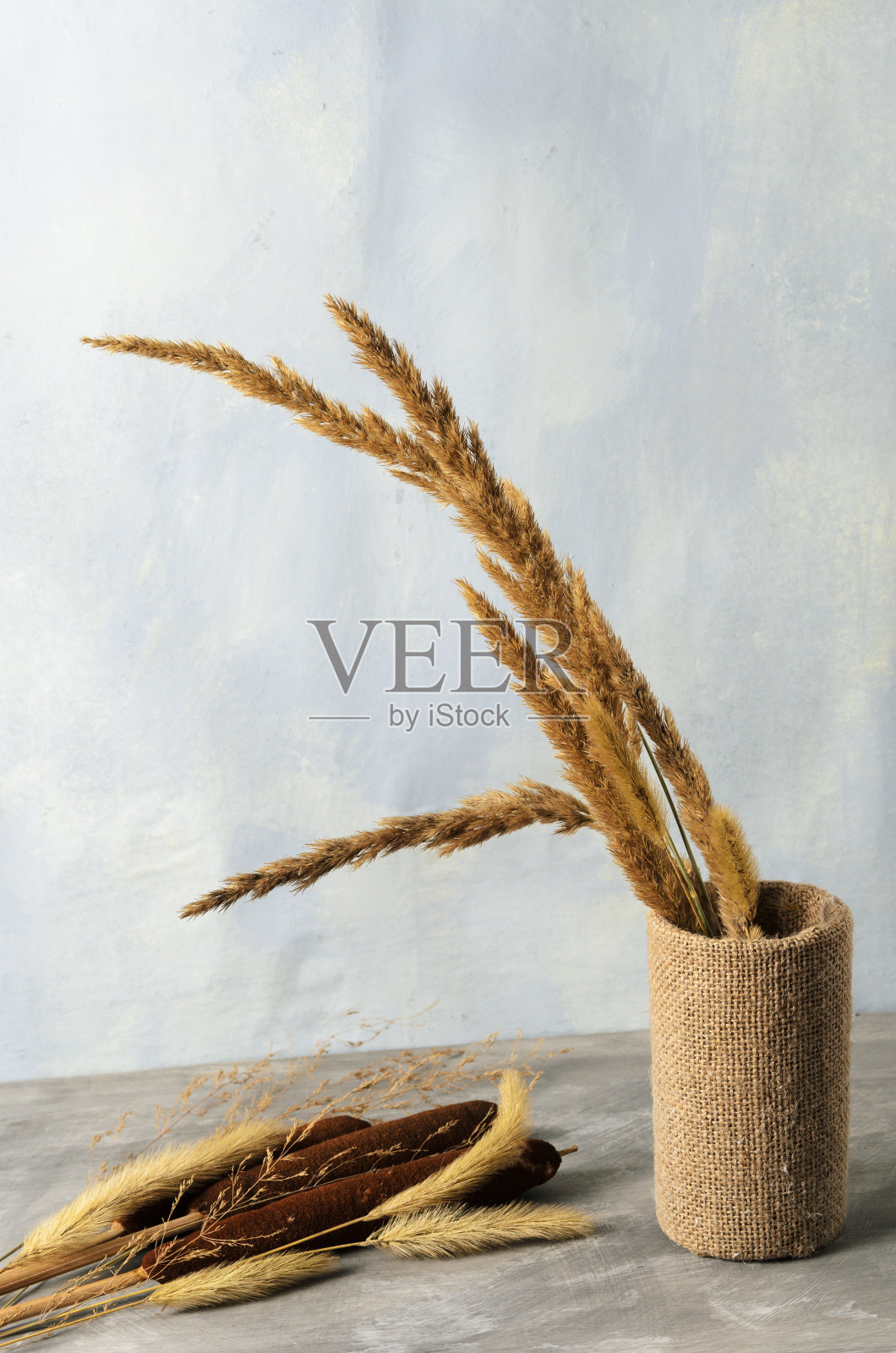 在灰色的混凝土表面和模糊的纹理背景上，装饰花瓶里放着一束干燥蓬松的草和芦苇小穗。照片摄影图片