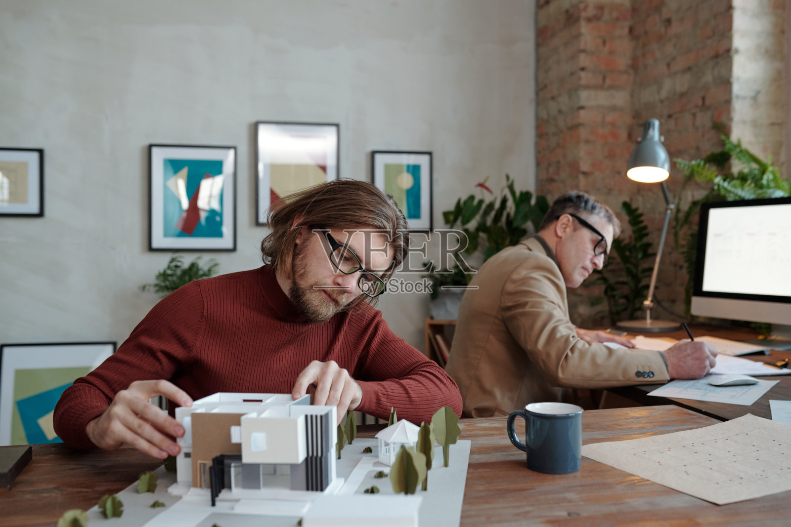 年轻严肃的男建筑师戴着眼镜和成熟的同事一起研究新房子模型照片摄影图片