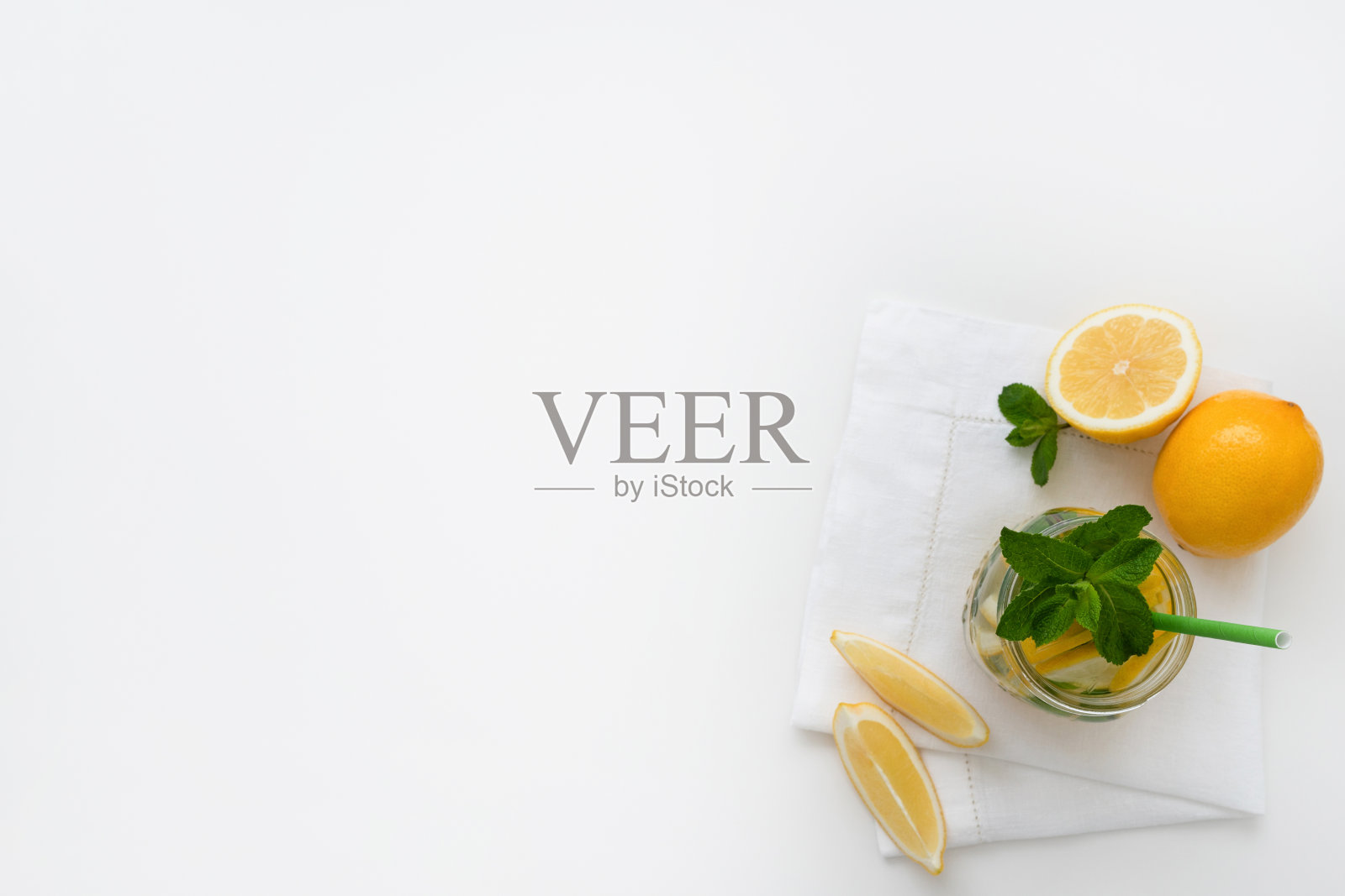 将柠檬水放在玻璃罐中，在白色餐巾上放上纸吸管、柠檬片和薄荷。照片摄影图片