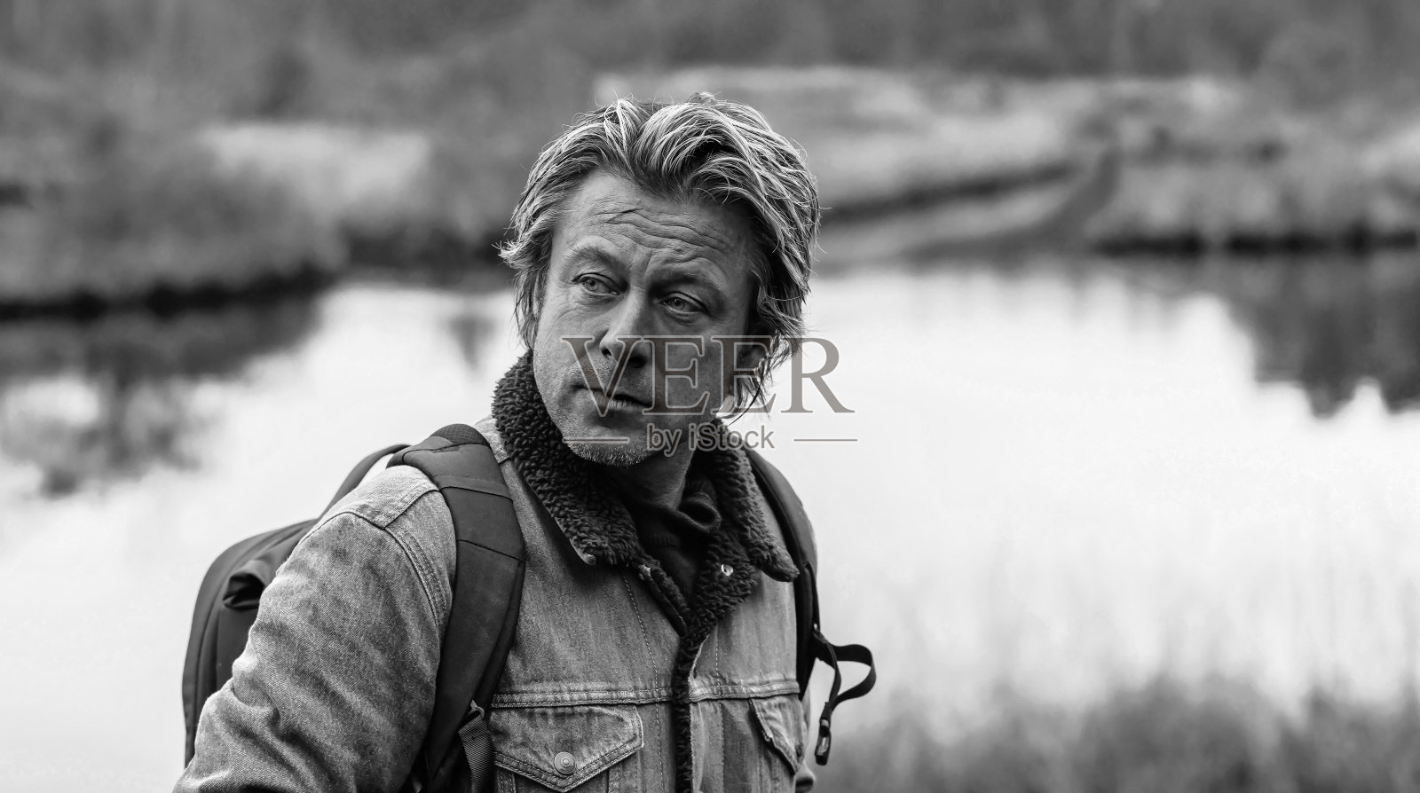 在湖边穿着牛仔裤夹克背着背包的男人。黑白粉照片摄影图片