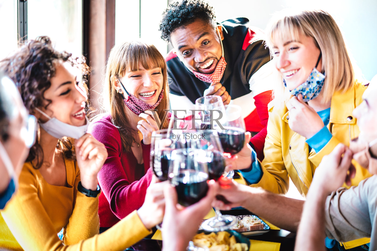 多种族的朋友在餐厅酒吧喝红酒，戴着开放的面罩-新的正常生活方式概念与快乐的人一起在关闭后重新开放-明亮生动的滤镜照片摄影图片