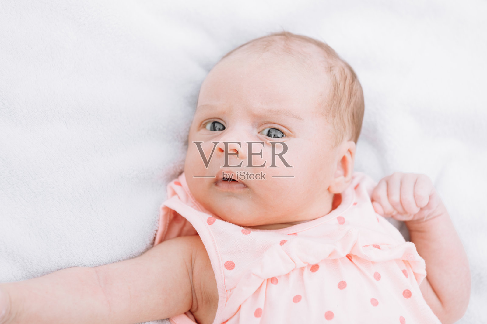 刚出生的女婴躺在公园外面的草地上，躺在白色的毯子上四处张望。有选择性的重点。照片摄影图片