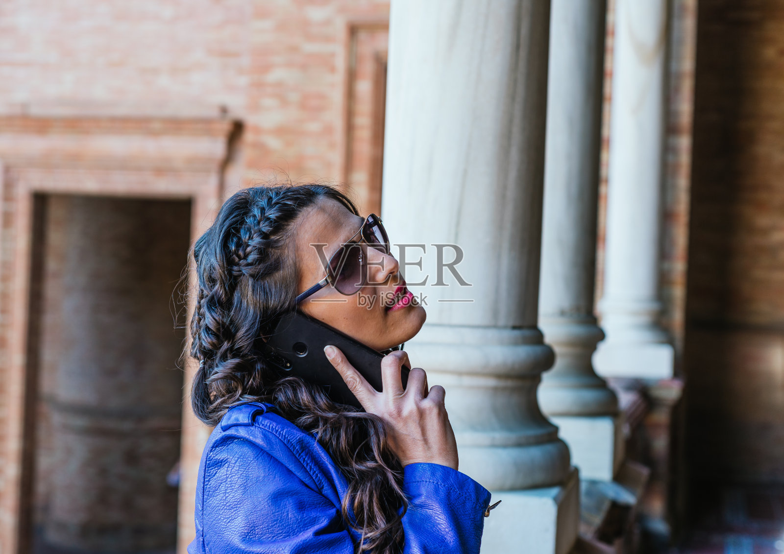 有魅力的女孩戴着太阳镜，穿着蓝色夹克在打电话照片摄影图片