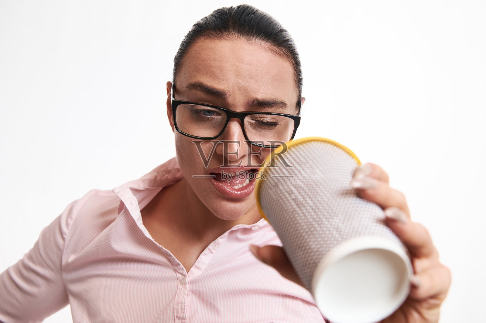 戴眼镜的困惑女人透过外卖纸杯，表达惊讶和不满。特写，白色背景，复制空间照片摄影图片