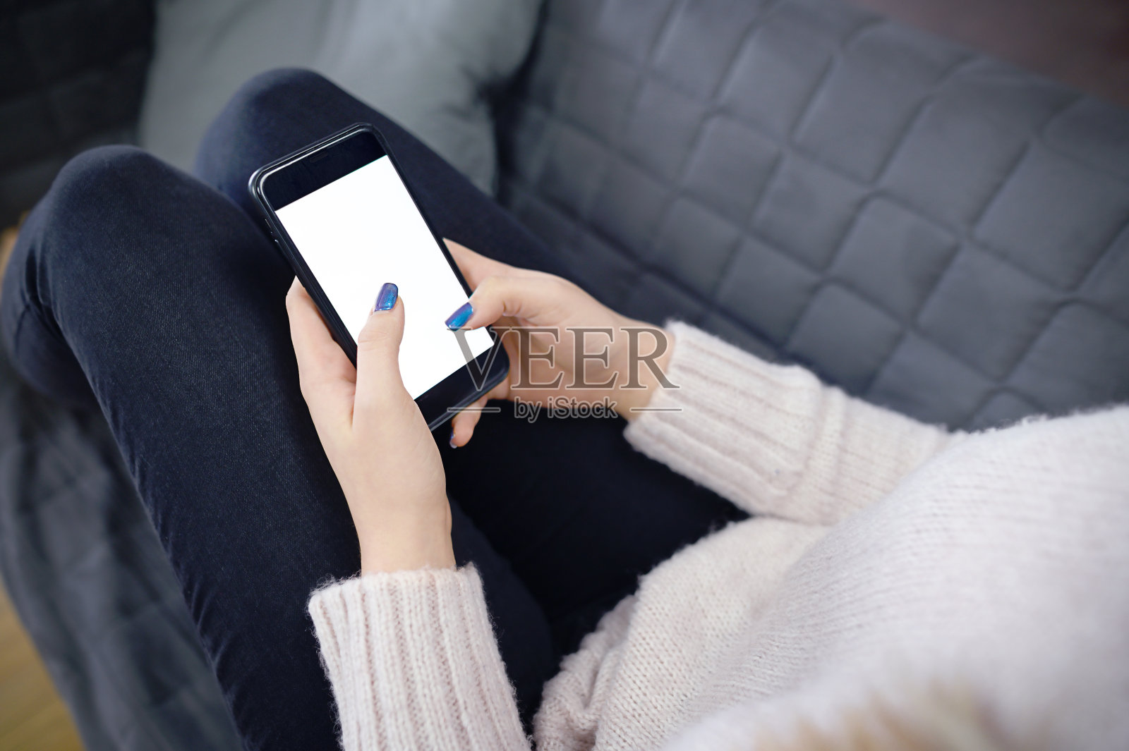 一个女人的后视图近距离握住和使用智能手机与白色空白空白屏幕坐在家里的床上。照片摄影图片