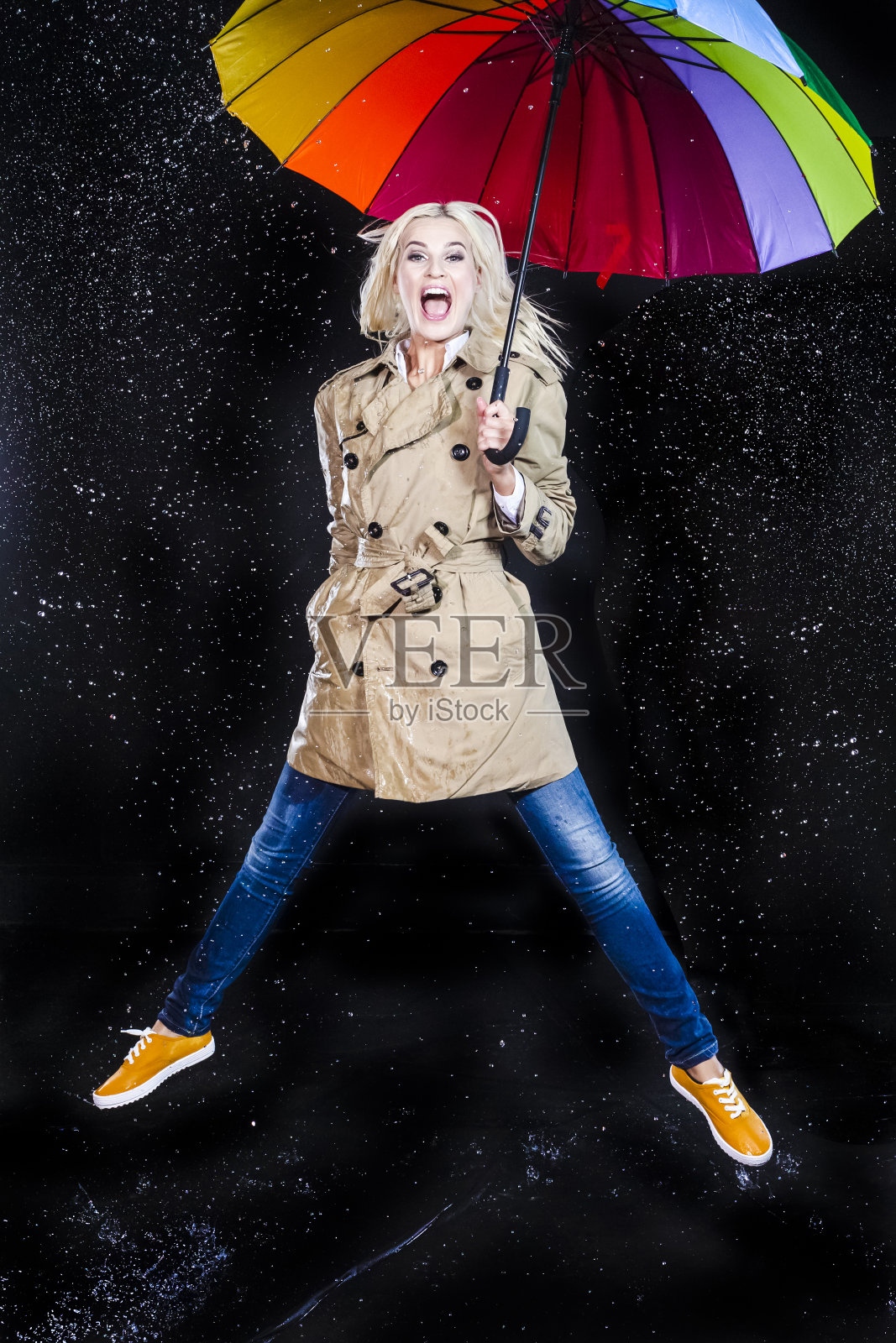 全长Portarit微笑的白种人金发女性跳跃与五颜六色的伞下的多个水滴。垂直的形象定位照片摄影图片