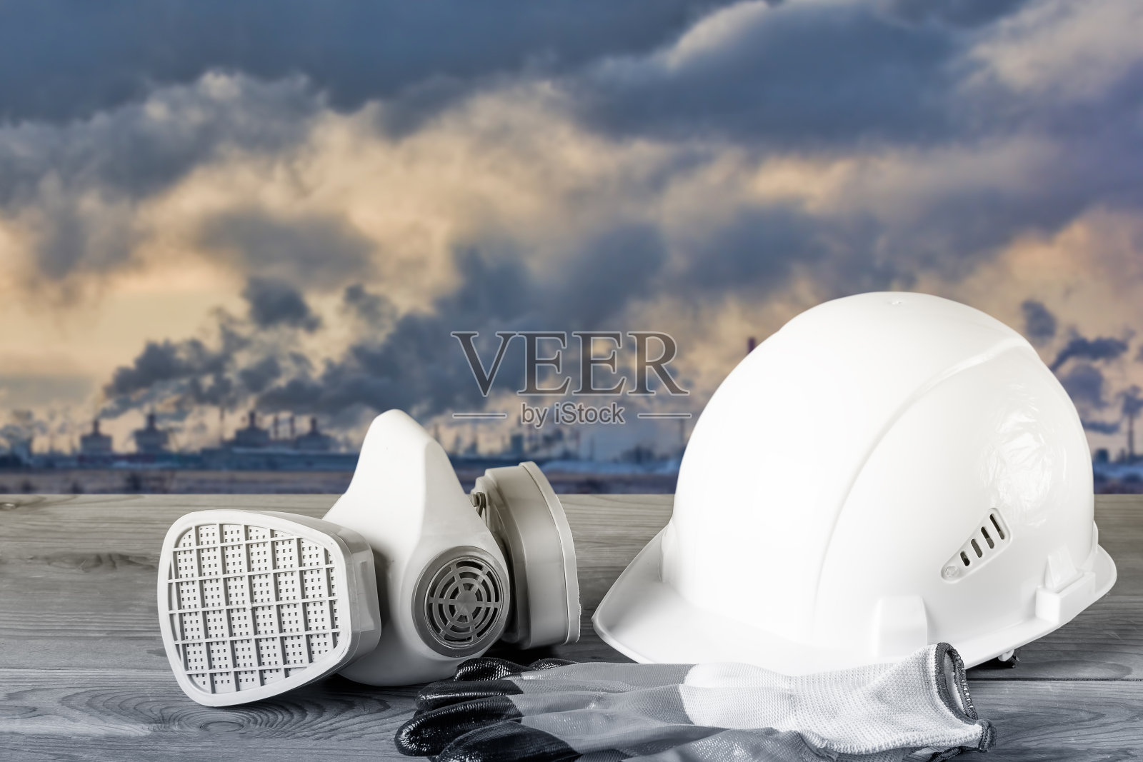 白色的防护头盔，呼吸器和工作手套，背景是一个化工厂的烟囱。工作场所安全的概念。照片摄影图片