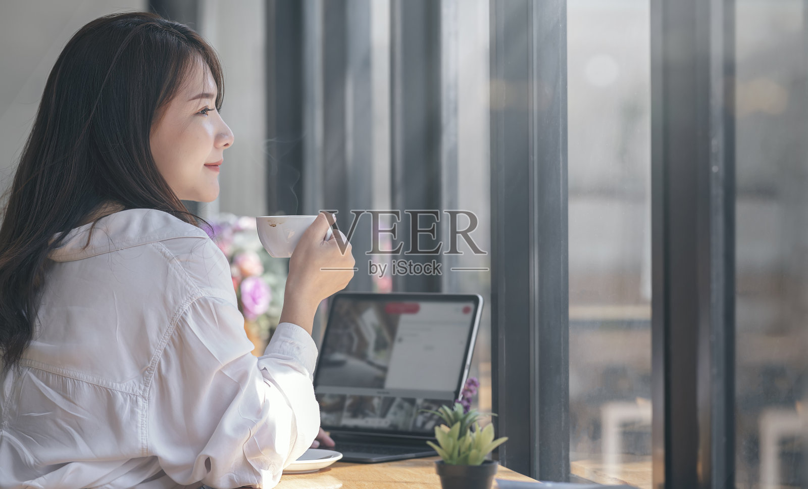 肖像年轻美丽的亚洲女人喝热咖啡，而坐在桌子在咖啡馆的房间。照片摄影图片