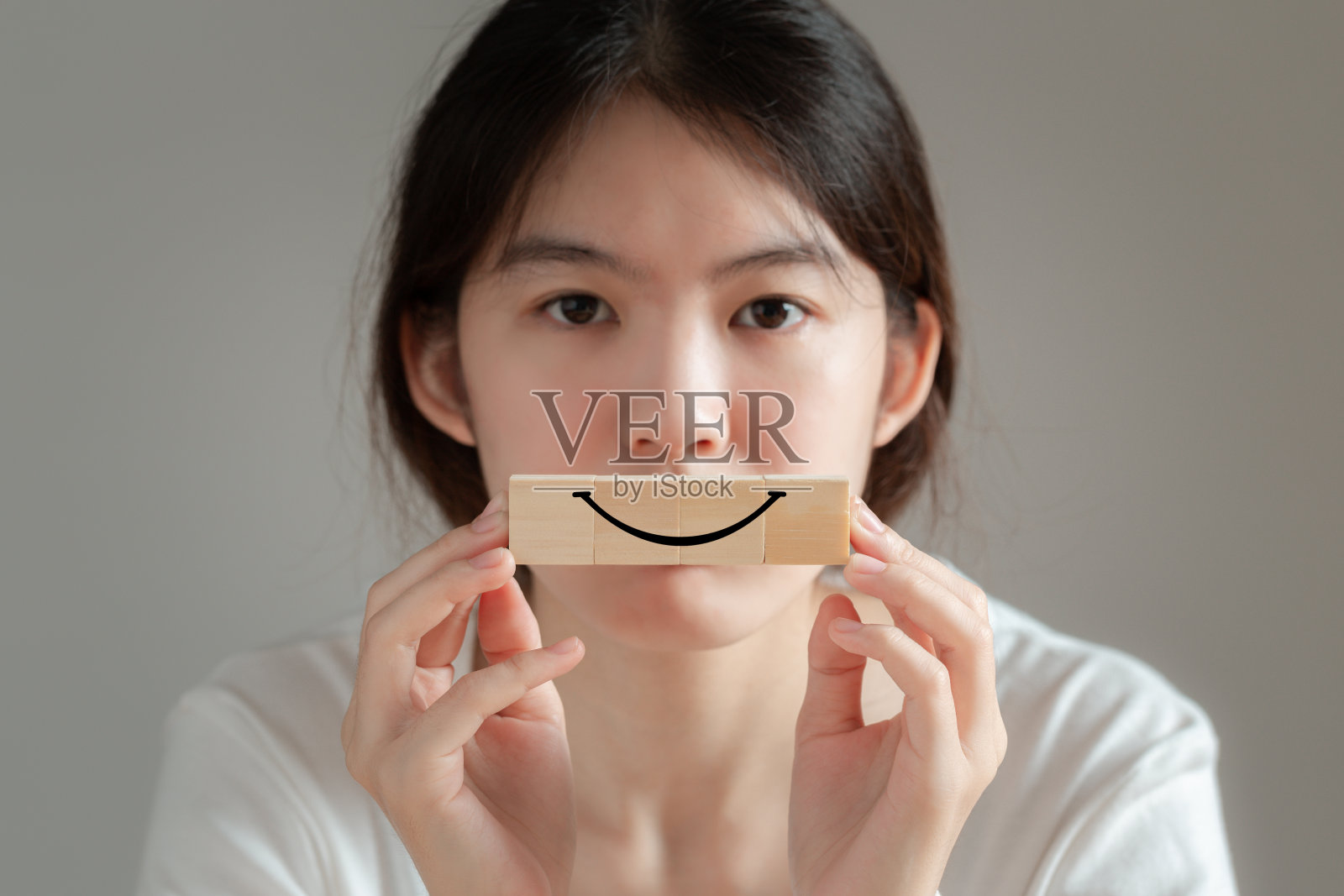 木方块上的笑脸符号。亚洲妇女拿着一个带有笑脸符号的木块来表达她的感情。照片摄影图片