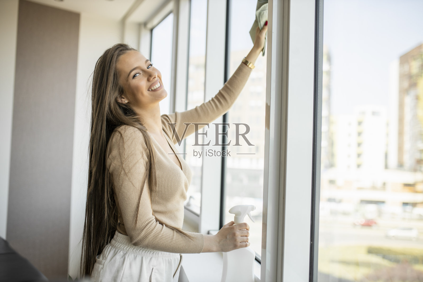 美丽的微笑年轻女子清洁和擦窗户用喷雾器和抹布照片摄影图片