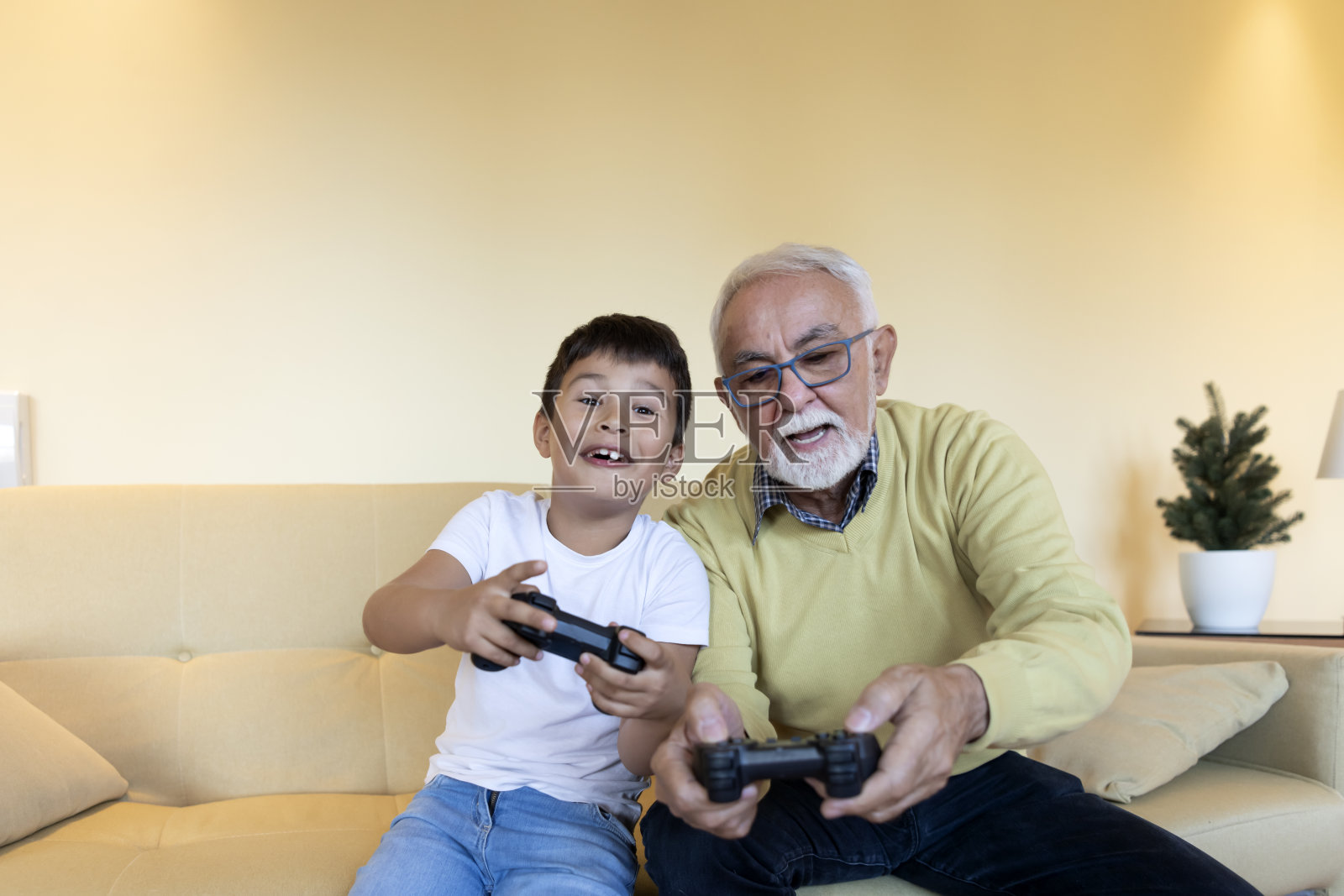 一个可爱的小孩和他的爷爷在家里玩电子游戏。照片摄影图片