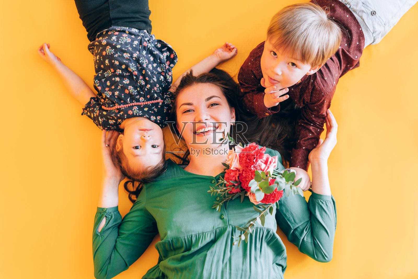 妈妈带着孩子躺在黄色的背景上。和孩子们在家玩游戏照片摄影图片