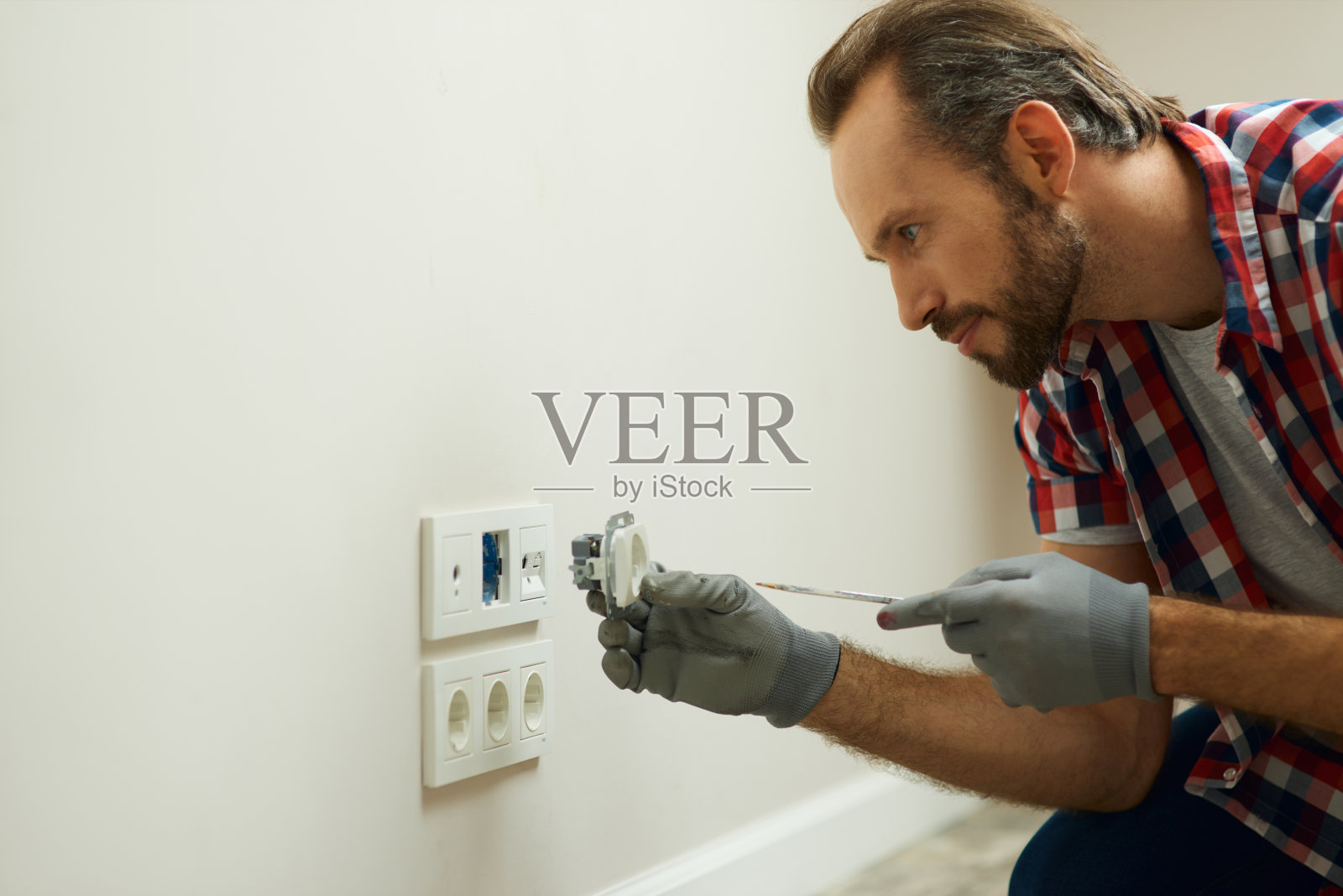 照片中的电工戴着防护手套，使用螺丝刀安装新的插头插座照片摄影图片